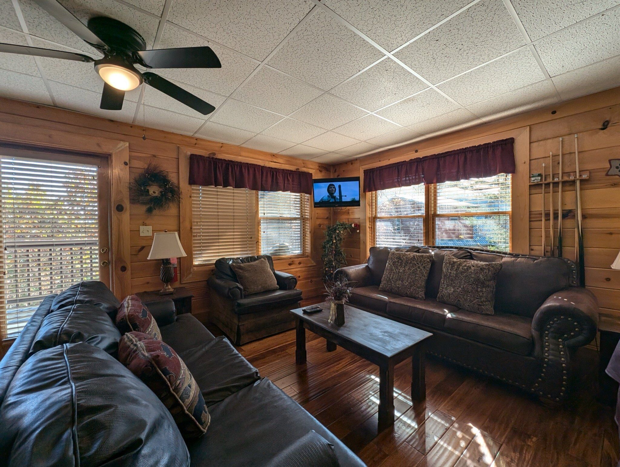 A cozy cabin interior with a wooden interior, a ceiling fan, a television, and a fireplace.