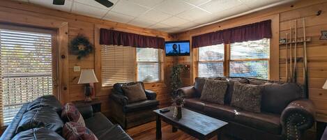 A cozy cabin interior with a wooden interior, a ceiling fan, a television, and a fireplace.