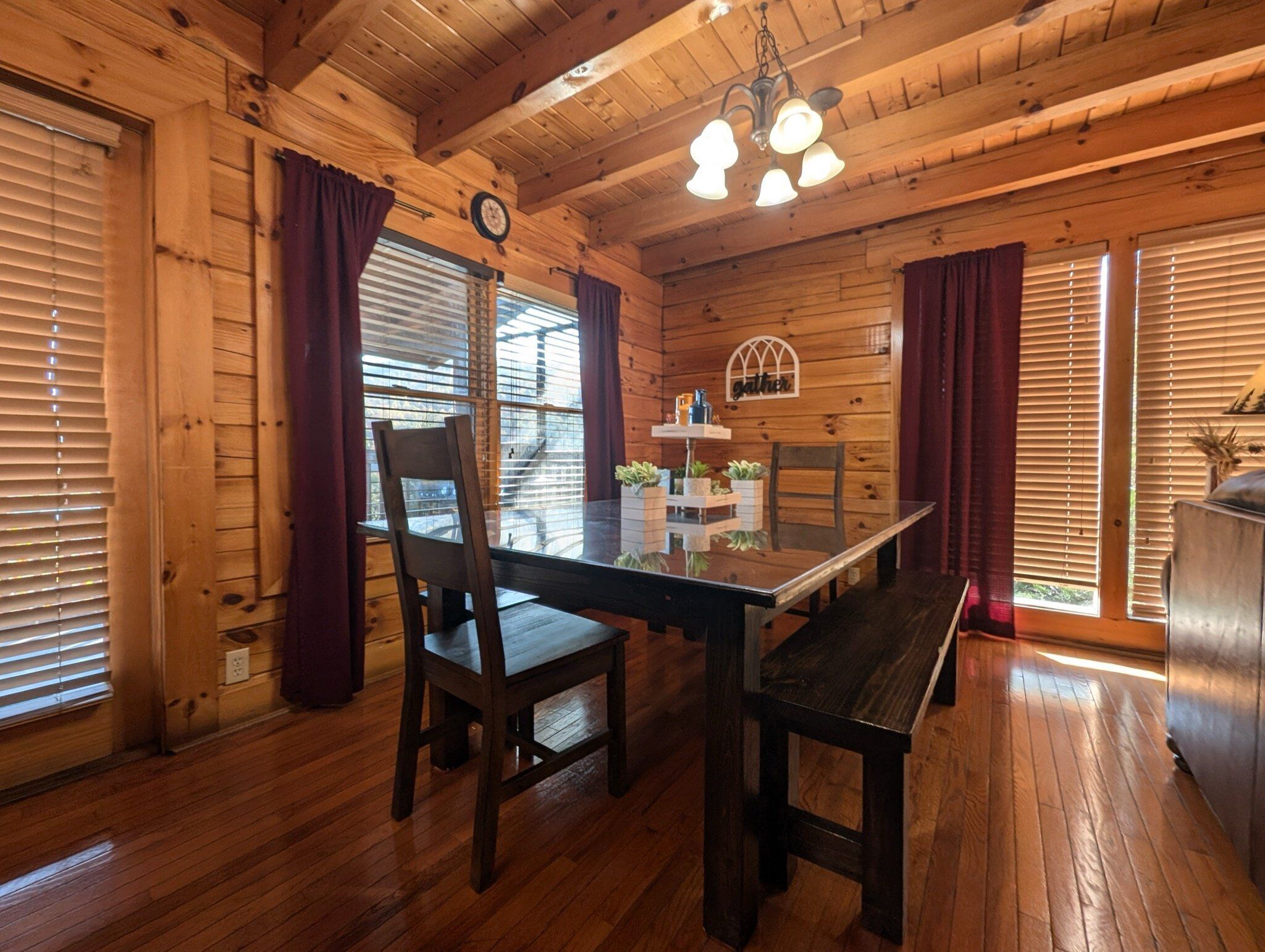 A wooden cabin interior with a dining table, chairs, a clock, and a chandelier.