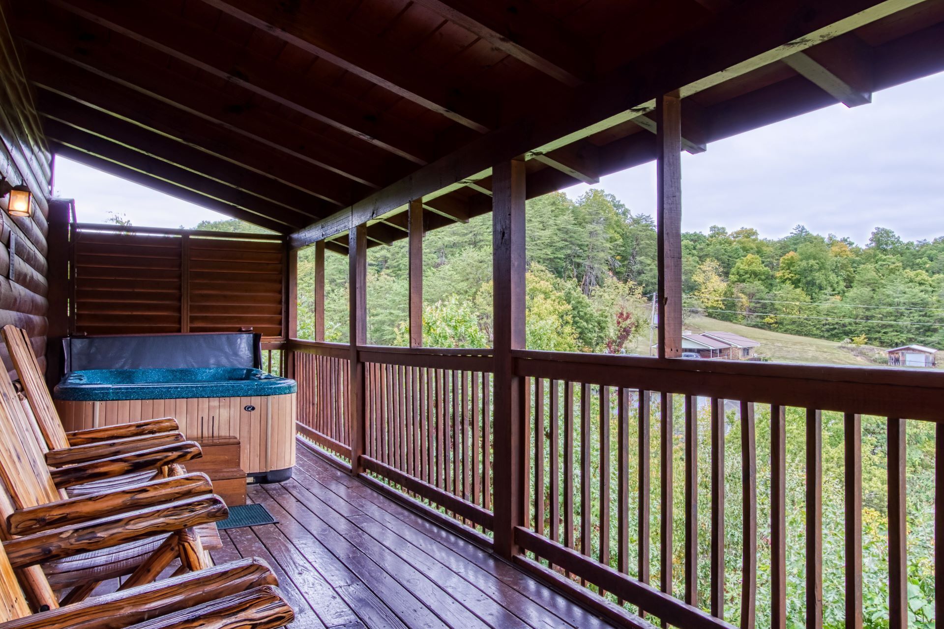 A wooden deck with a hot tub, wooden chairs, and a view of a forested area.