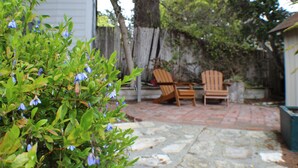 Un patio con suelo de piedra, dos sillas de madera y una valla de madera al fondo.