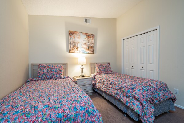 A bedroom with two beds, a nightstand with a lamp, a painting on the wall, and a closet.