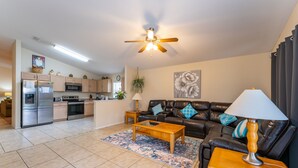 A modern living room with a sofa, coffee table, and lamp, connected to a kitchen with appliances and a dining area. - Budget Friendly! Lake View Home with a Private pool nearby to Disney (Davenport)