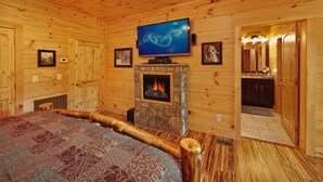 A cozy log cabin room with a fireplace, a television mounted above it, and a bed with a patterned bedspread.