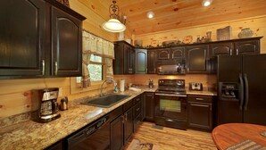 A kitchen with dark wooden cabinets, a granite countertop, a coffee maker, a sink, a stove, and a refrigerator.