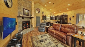 A cozy cabin interior with a stone fireplace, leather sofa, and a dining area.