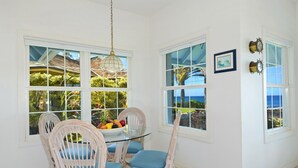 A dining area with a glass table and wicker chairs, overlooking a tropical garden and ocean view. - Home Of The Cherished Seacoast By Parrish Kauai- oceanfront & walk to Poipu Beac (Koloa)