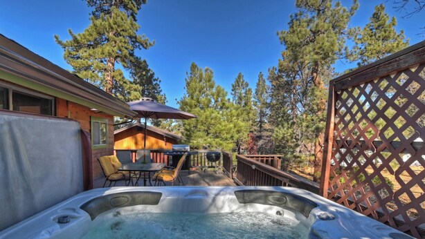 Un jacuzzi en un patio trasero con una terraza de madera, una parrilla y una mesa de comedor con sillas.