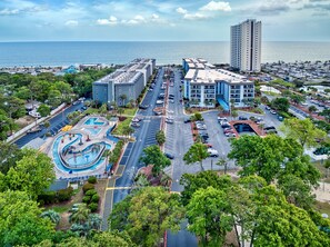 A hotel with a swimming pool, parking lot, and a view of the ocean.
