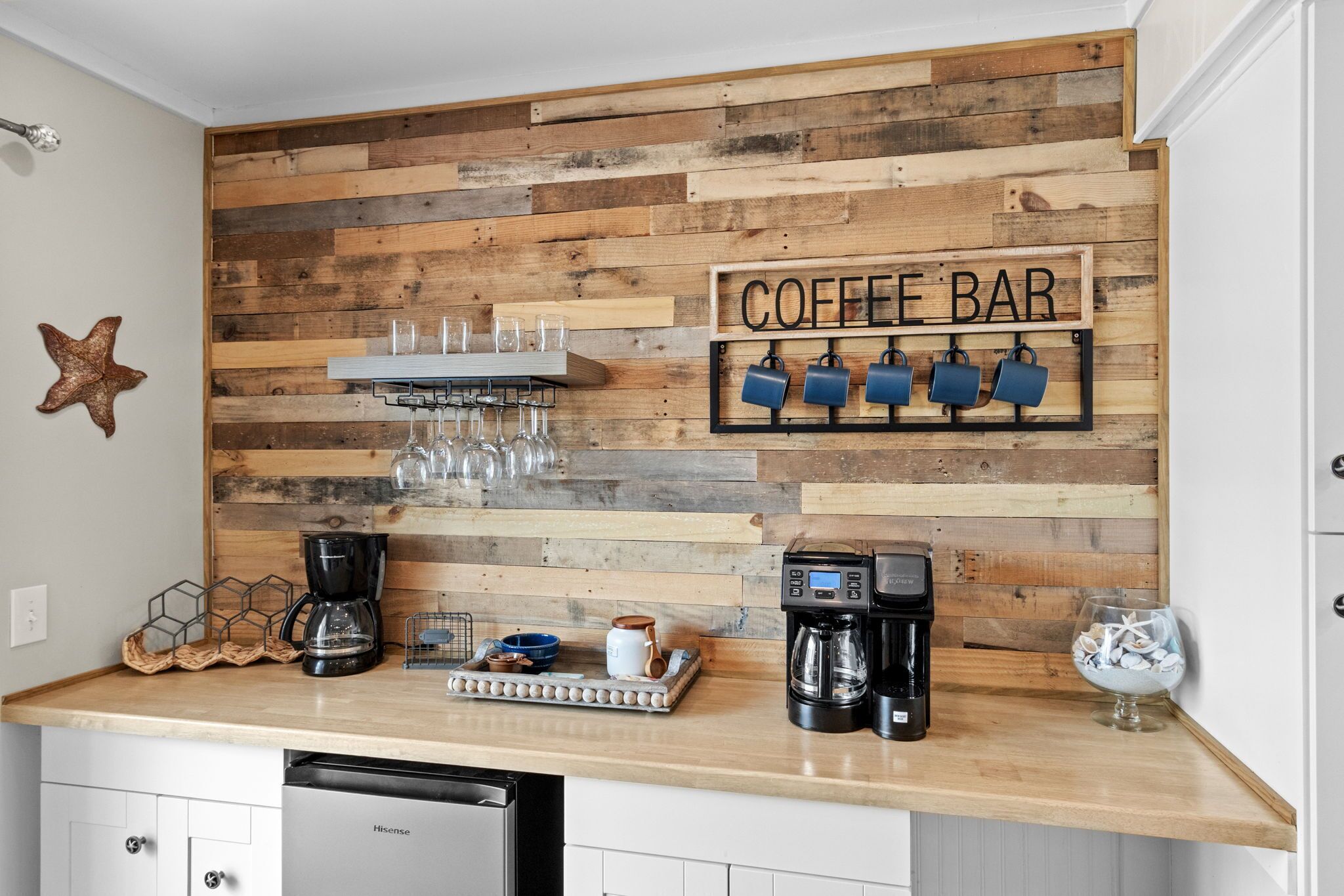 A kitchen with a wooden wall, coffee bar sign, coffee machines, and a starfish decoration.