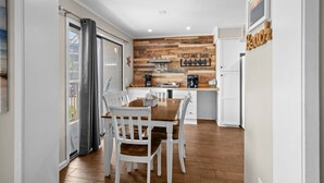 A modern kitchen with a wooden accent wall, a coffee bar, and a dining area with white chairs. - A114 at the Myrtle Beach Resort (Myrtle Beach)