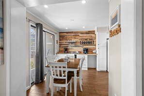 Una cocina moderna con un muro de acento de madera, una barra para café y una zona de comedor con sillas blancas.