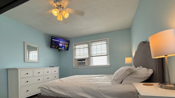 Un dormitorio con cama, cómoda, televisor montado en la pared y ventilador de techo.