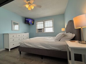 A bedroom with a bed, a dresser, a TV mounted on the wall, and a ceiling fan.