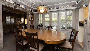 A dining area with a large wooden table surrounded by chairs, a chandelier, and a view through large windows. - 359CA: Charming Family Home, 3 Blocks to Beach, Restaurants and Shops (Avalon)