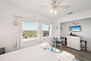 A bedroom with a bed, a chair, a dresser, a television, and a ceiling fan.