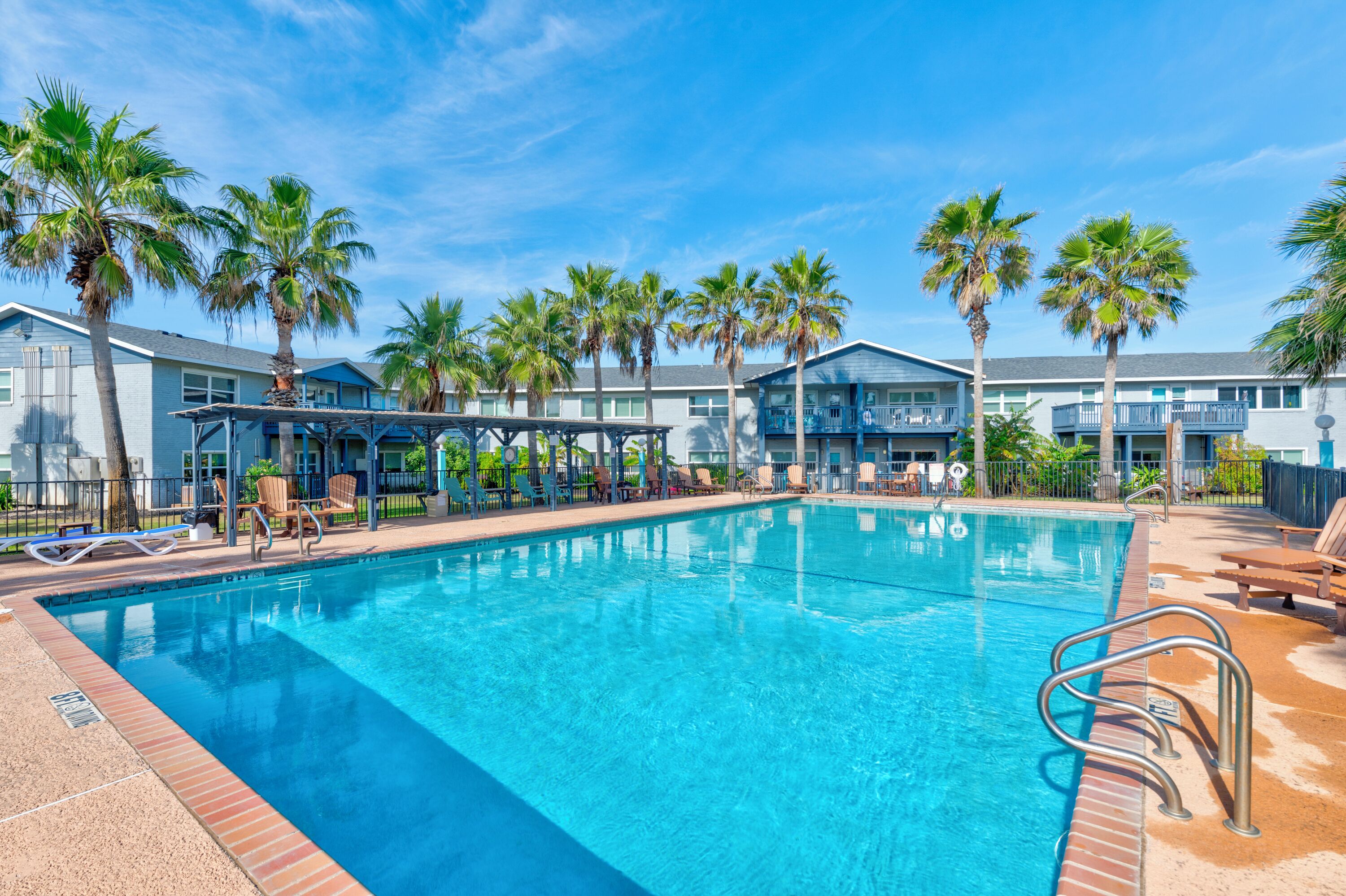 Ein Pool mit Liegestühlen und Palmen, umgeben von Gebäuden mit Balkonen.