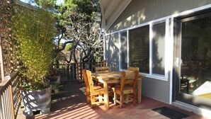 An outdoor patio with a wooden table and chairs, surrounded by a wooden deck and a metal fence.