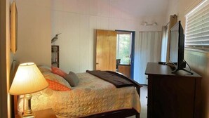 A bedroom with a bed, a lamp, a TV, and a window.