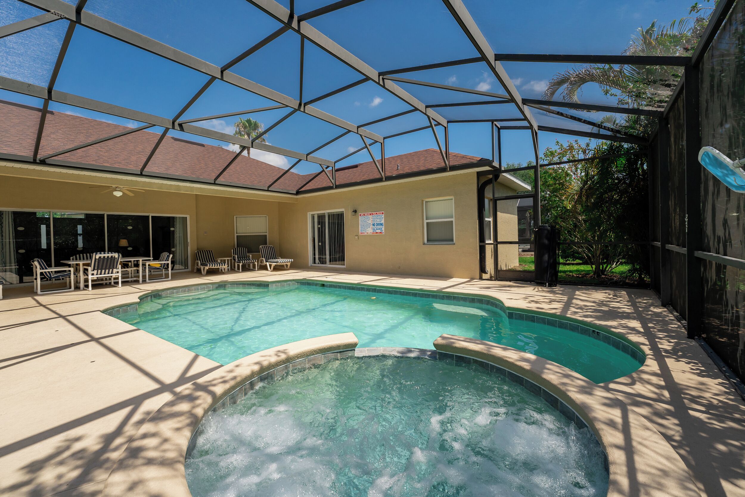 A swimming pool with a hot tub, surrounded by lounge chairs and a covered patio area.