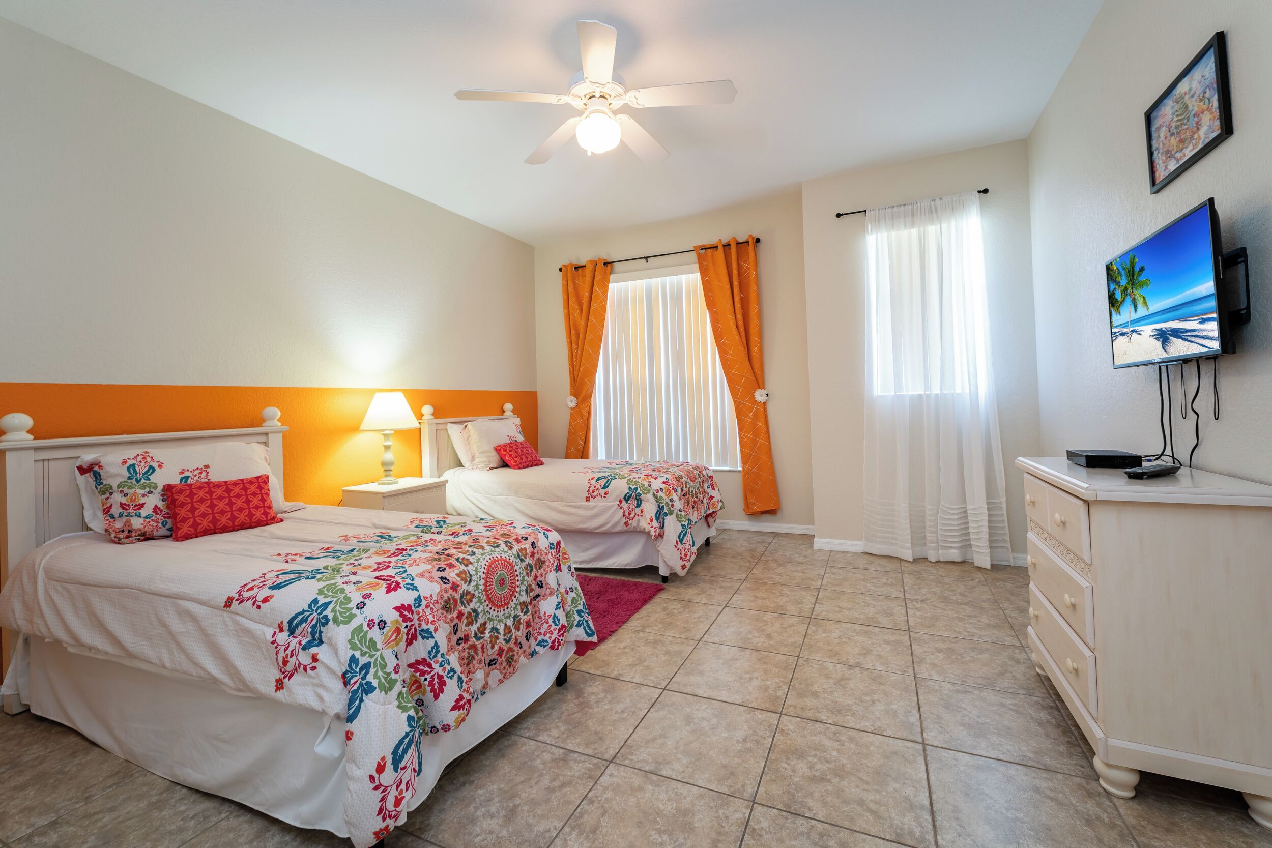 A bedroom with two beds, a ceiling fan, a TV, and a dresser.