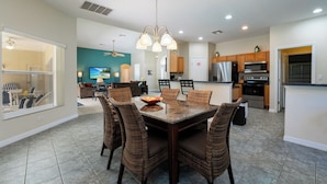 A modern kitchen with a dining area, featuring a large island, built-in appliances, and wicker chairs.