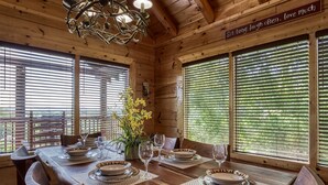 Una sala da pranzo in legno con un tavolo apparecchiato per quattro persone, ampie finestre con persiane e un lampadario.