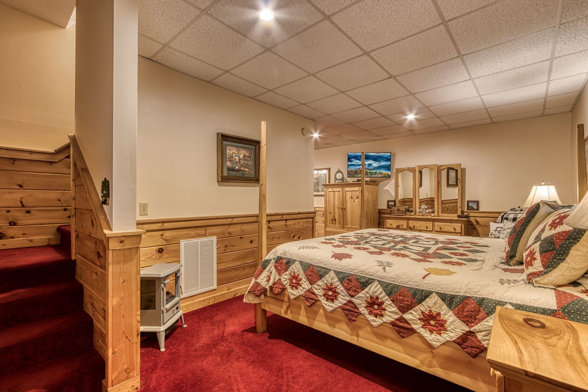 A bedroom with a wooden bed, a red carpet, a wooden dresser, a mirror, and a television.