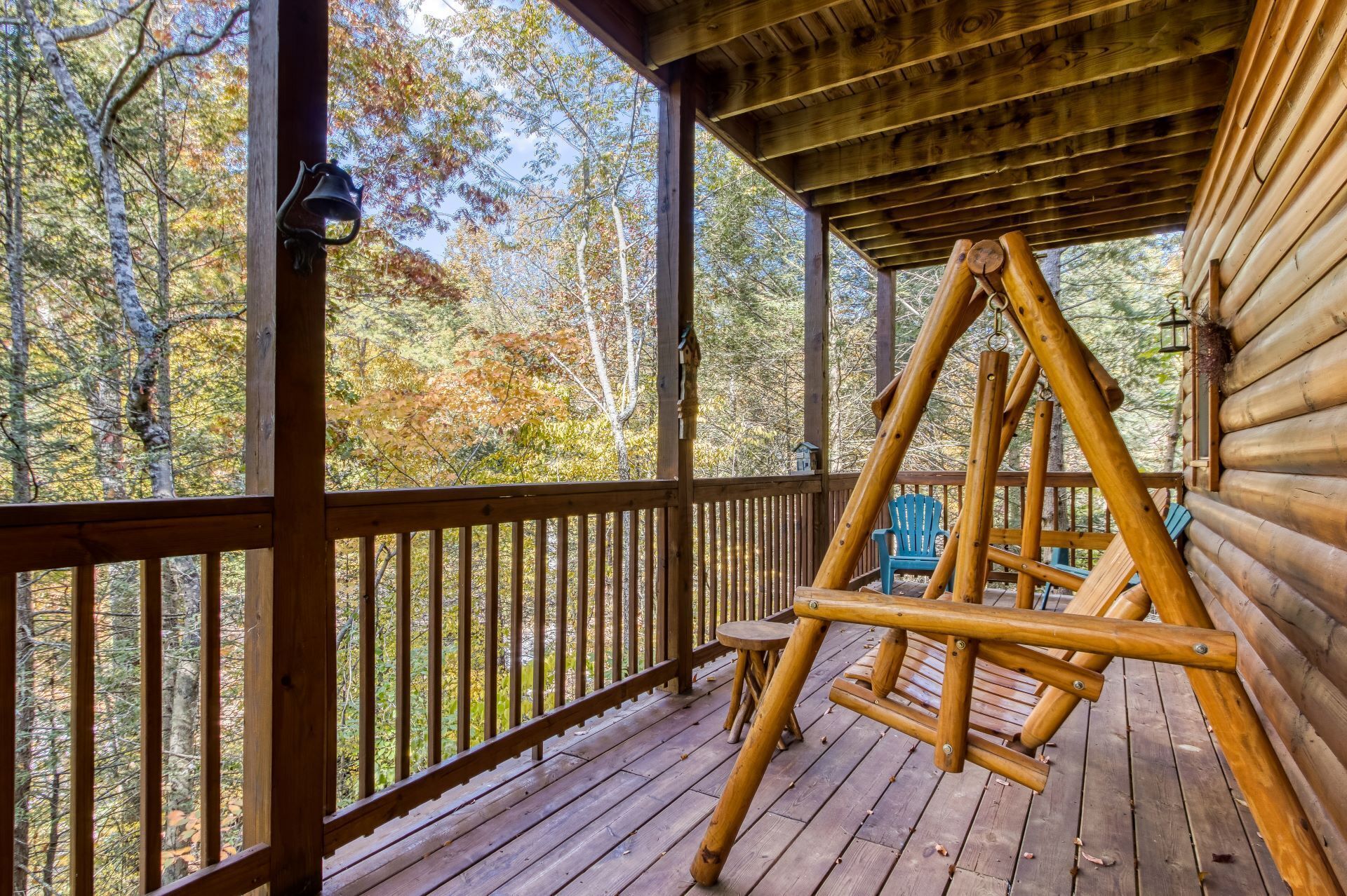 Une terrasse en bois avec une balançoire et une vue sur les arbres aux couleurs automnales.