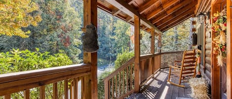 Una terraza de madera con barandilla, una mecedora y vistas a un bosque.