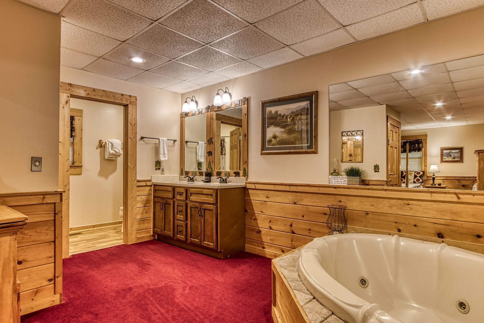 A bathroom with wooden paneling, a large bathtub, a vanity with a mirror, and a red carpet.