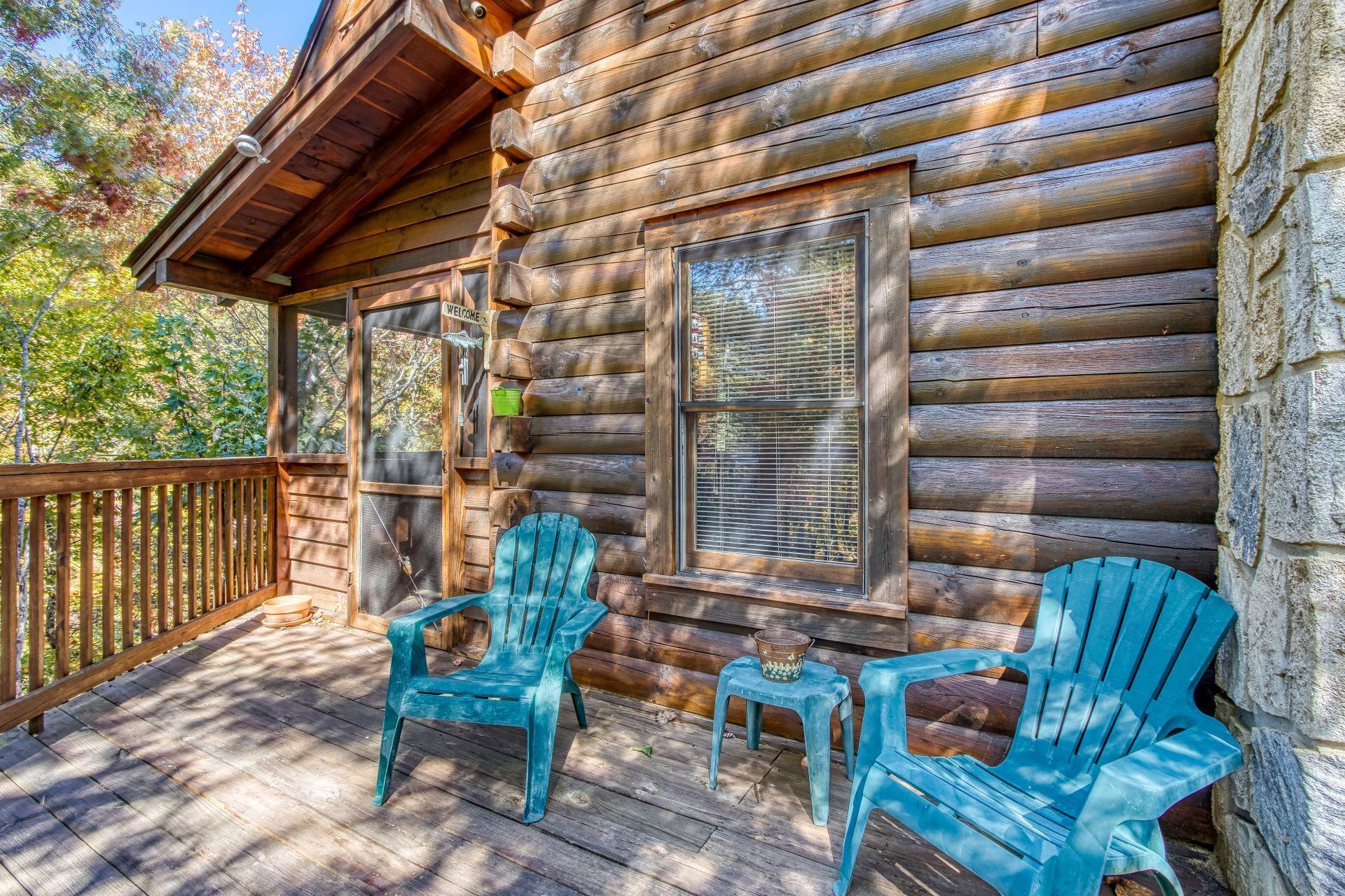 A wooden cabin with a porch, two turquoise Adirondack chairs, and a welcome sign.