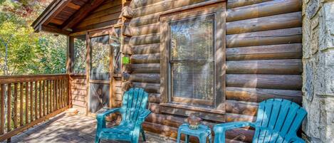 A wooden cabin with a porch, two turquoise Adirondack chairs, and a welcome sign.