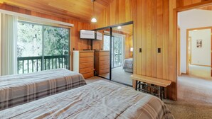 A wooden-paneled room with two beds, a TV, and a sliding glass door leading to an outdoor balcony. - BACK03 - Walk to Sunriver Village! Quiet Setting, 2 Suites, A/C, Hot Tub (Sunriver)