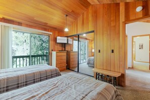 A wooden-paneled room with two beds, a TV, and a sliding glass door leading to an outdoor balcony. - BACK03 - Walk to Sunriver Village! Quiet Setting, 2 Suites, A/C, Hot Tub (Sunriver)