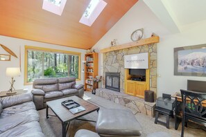 Un salon chaleureux avec une cheminée en pierre, des meubles en cuir et une grande fenêtre donnant sur une forêt.