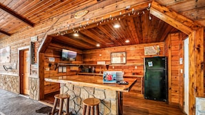 A wooden cabin with a bar area, stone accents, and a refrigerator. - POOL | Basketball | 6 bdrm | Theater | Acreage! (Gatlinburg)