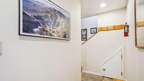 Un pasillo con un cuadro grande enmarco, un extintor montado en la pared y un banco de madera.