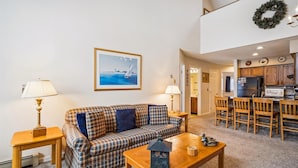 A living room with a plaid sofa, a wooden coffee table, and a painting of a sailboat. - Charming 2-Bedroom Slopeside Condo at Pico Mountain E304 (Killington)