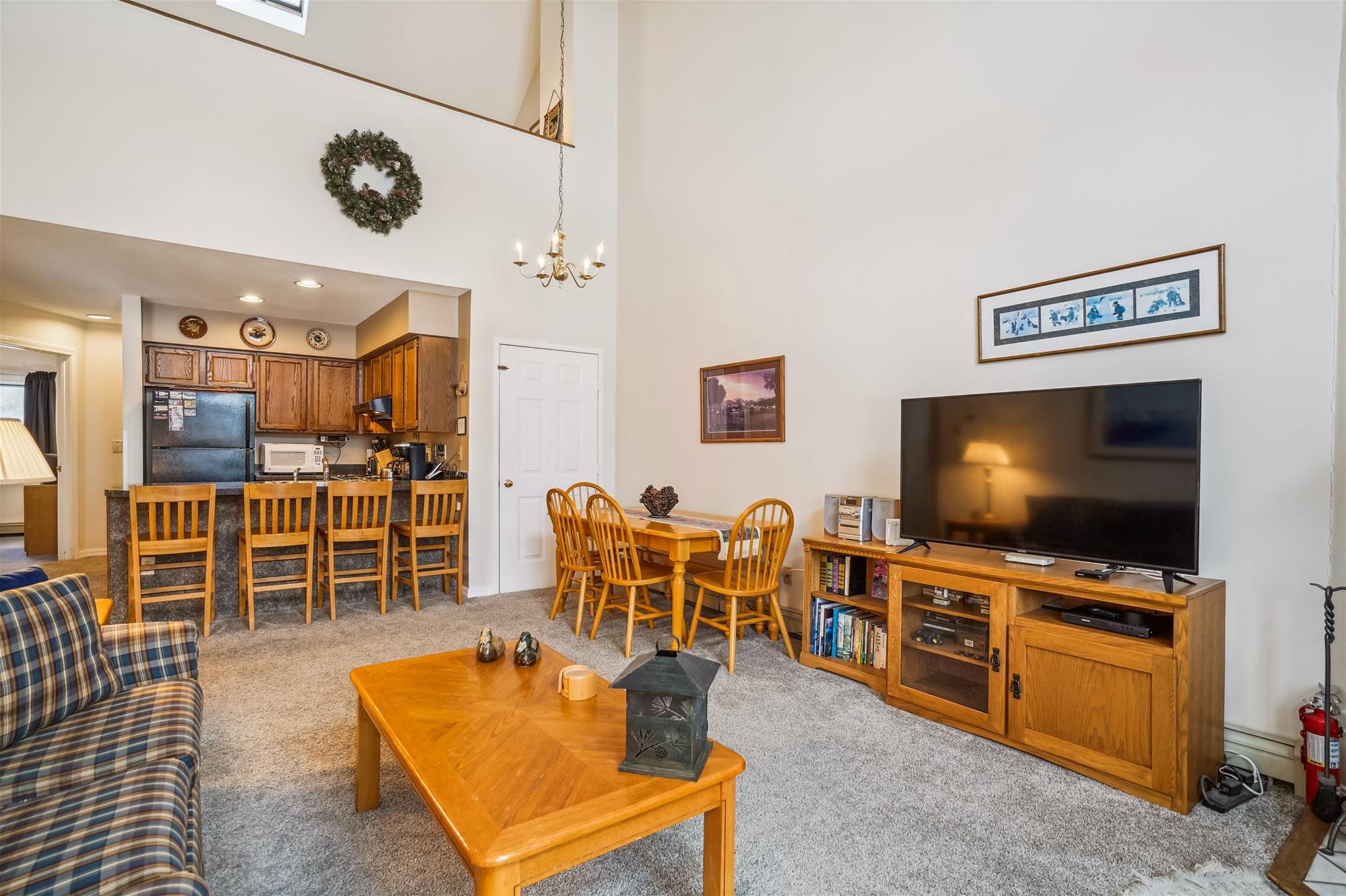 A living room with a TV, wooden furniture, a fireplace, and a kitchen in the background.