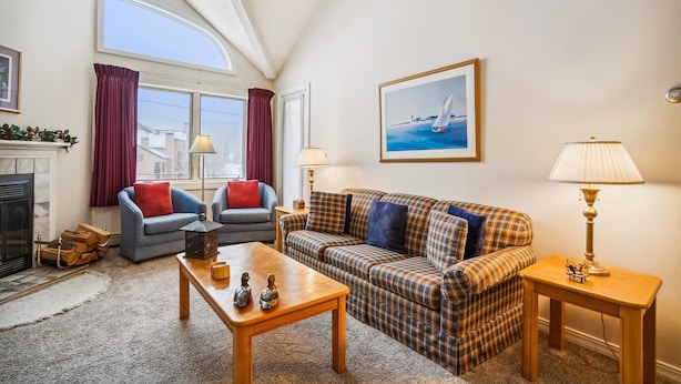 A living room with a fireplace, two armchairs, a sofa, a coffee table, and a painting of a sailboat. - Charming 2-Bedroom Slopeside Condo at Pico Mountain E304 (Killington)