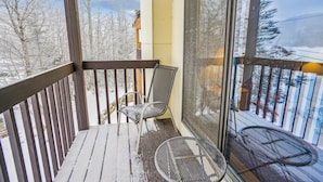 A covered balcony with a chair and a small table, overlooking a snowy landscape. - Charming 2-Bedroom Slopeside Condo at Pico Mountain E304 (Killington)