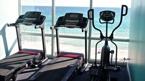 Drei Trainingsgeräte mit Blick auf den Ozean durch große Fenster.