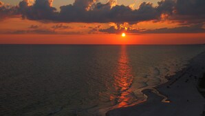 Ein Sonnenuntergang über einem Strand, wobei sich die Sonne im Wasser spiegelt.