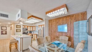 Une cuisine moderne avec des meubles en bois, un îlot central et un coin repas agrémenté de chaises en osier et d’une table en verre.