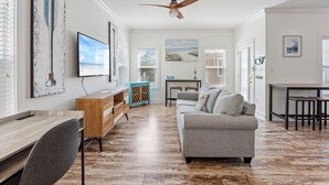 A spacious living room with a wooden floor, a grey sofa, a wooden desk, and a ceiling fan.