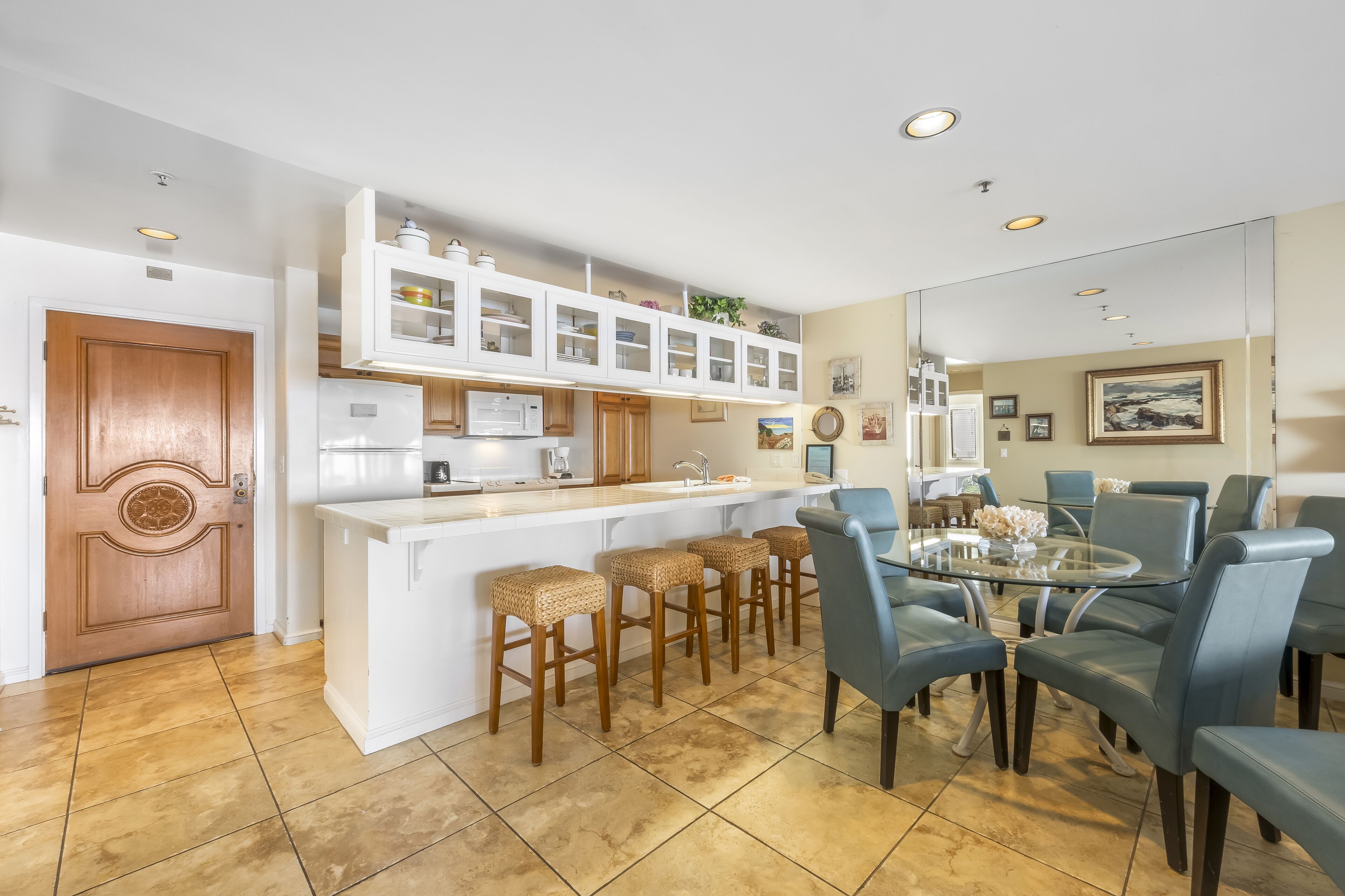 A modern kitchen with white cabinetry, a central island with stools, and a dining area with blue chairs.