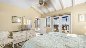 Une chambre avec un lit, une commode, une chaise et une vue sur la plage, accessible par une porte coulissante.