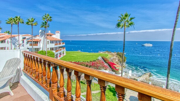 Un hôtel en bord de mer doté d’un balcon, de palmiers et offrant une vue sur l’océan.