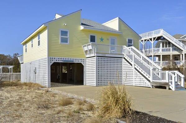 A yellow building with a white porch and a staircase leading to a deck.